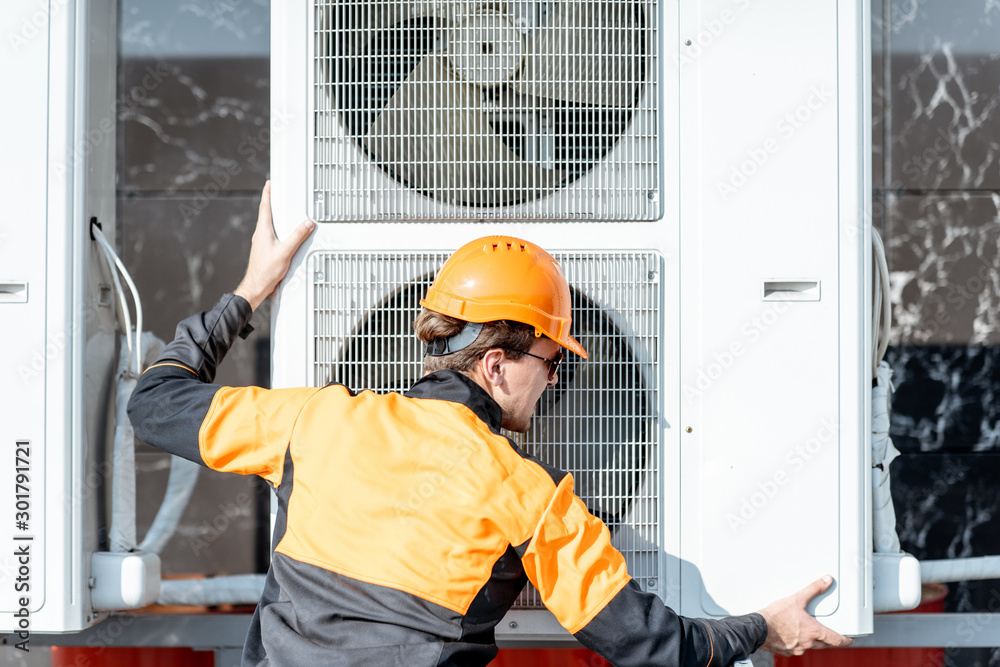 Professional workman in protective clothing installing outdoor unit of the air conditioner or heat pump on the rooftop