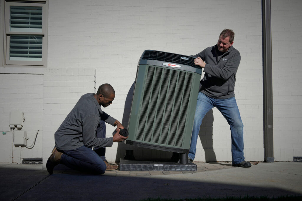 Two HVAC technicians servicing outdoor unit